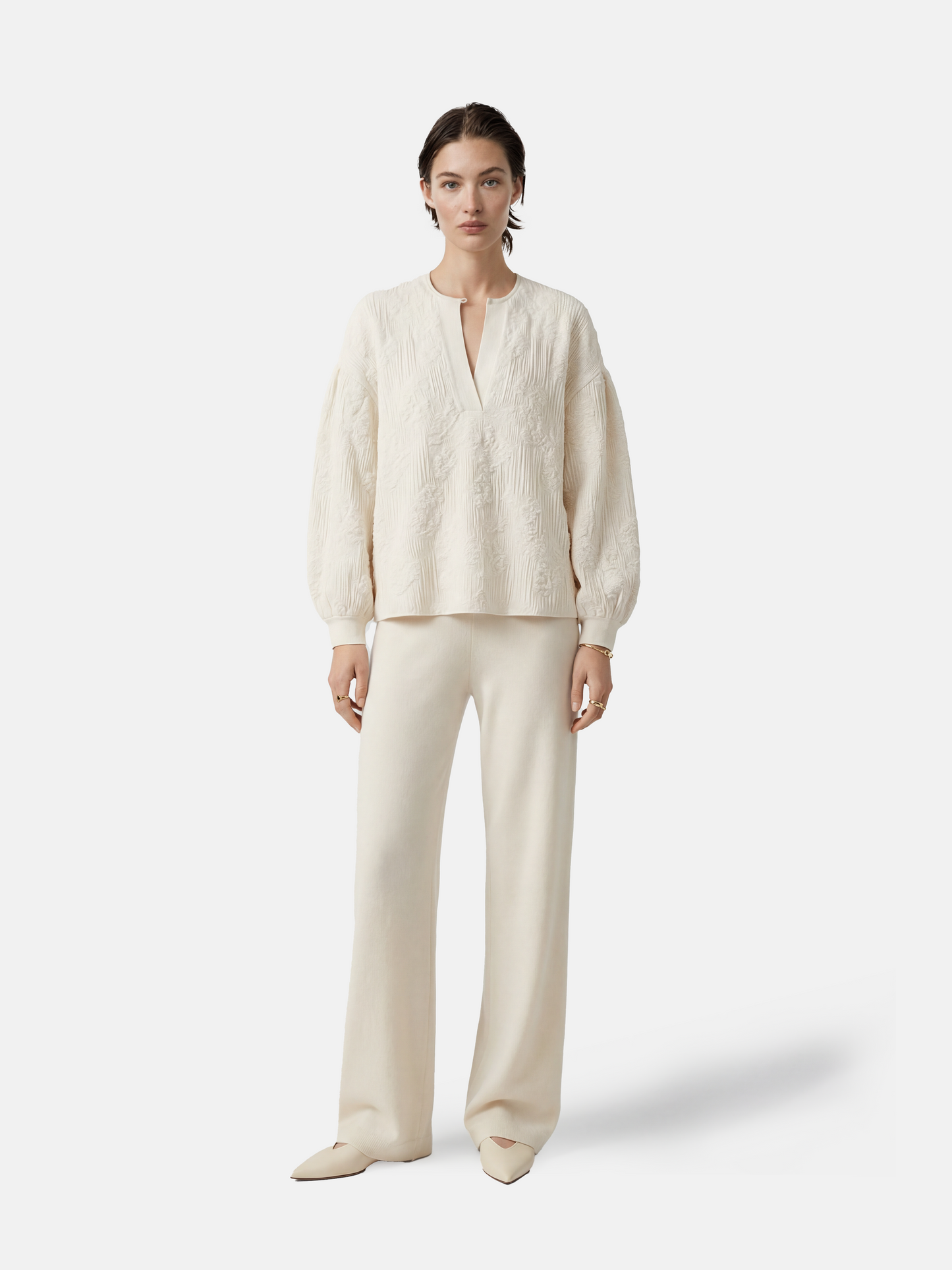 Relaxed ivory cashmere knit top featuring a clean round neck, deep slit, soft volume sleeves with neat cuffs, and a distinctive raised texture.