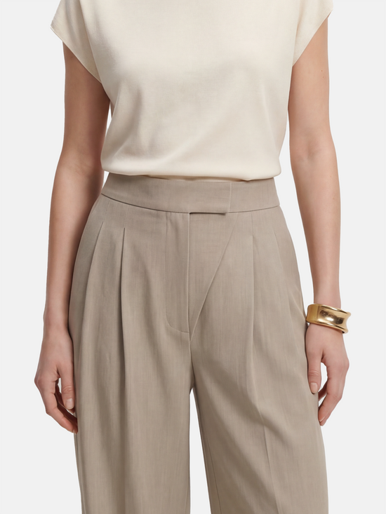 Cropped wide-leg trousers in quiet khaki, featuring deep pleats and an asymmetric front, embodying architectural form and fluid motion.