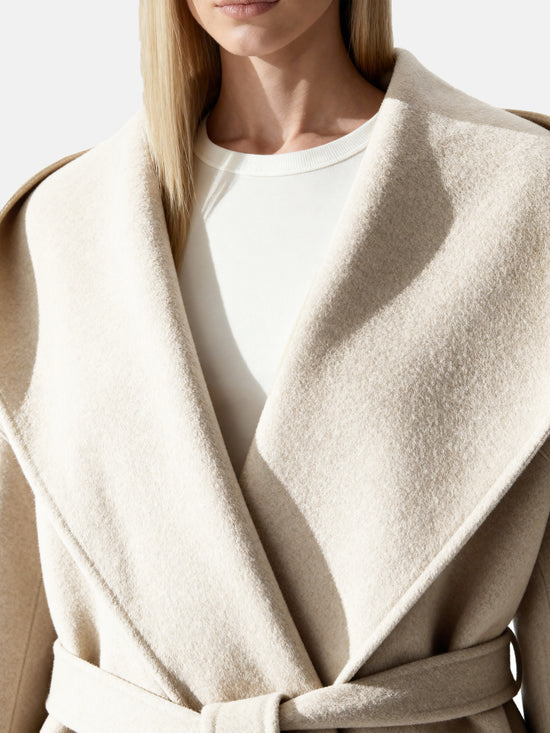 Full-length image of a cream wool belted overcoat with sculpted collar, self-tie belt, and oversized patch pockets, draped elegantly.