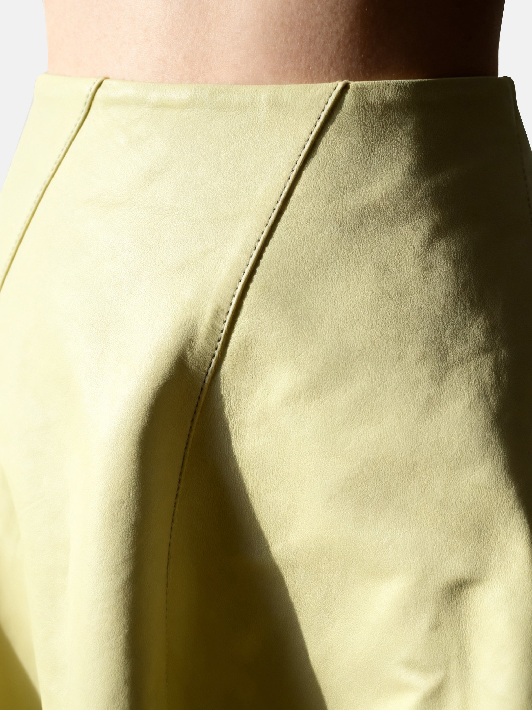 Soft yellow high-waist lambskin miniskirt with a gentle A-line silhouette, showcasing its supple texture and precise cut.