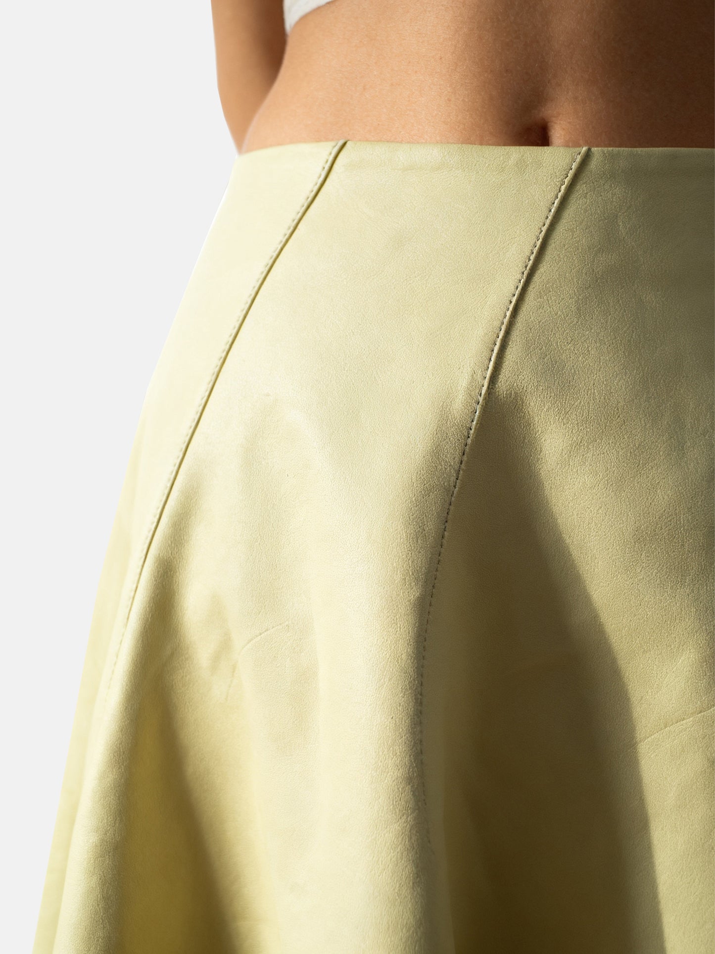 Soft yellow high-waist lambskin miniskirt with a gentle A-line silhouette, showcasing its supple texture and precise cut.