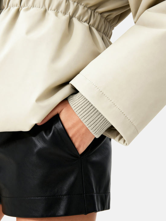 Apricot high-collar structured puffer down jacket by SELVANE, featuring a concealed placket and cinched waist, presented architecturally.