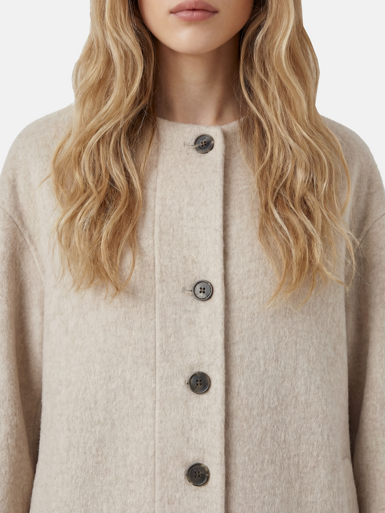 Beige wool and camel hair buttoned coat by SELVANE, featuring a rounded neck and minimal buttons, draped elegantly.