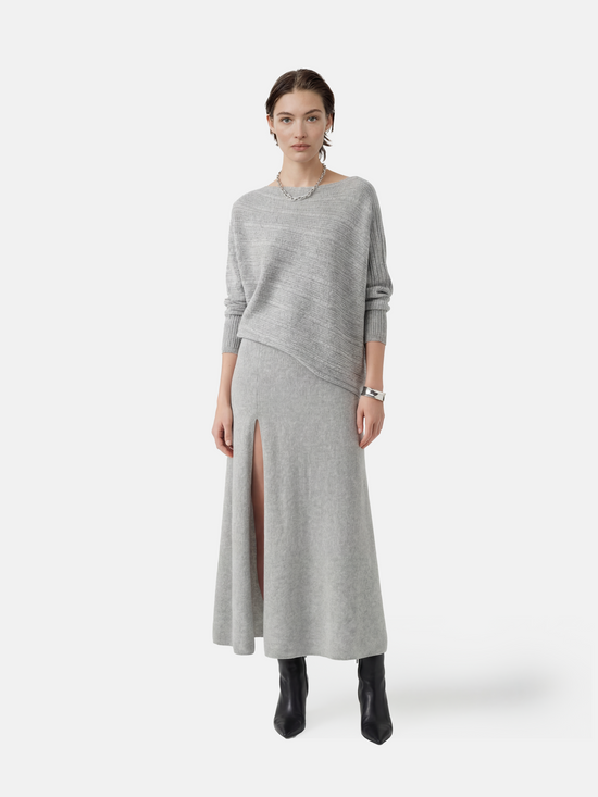 Cashmere draped knit top in grey with wide boat neckline and asymmetric hem, showcasing fluid motion and refined rib sleeves.