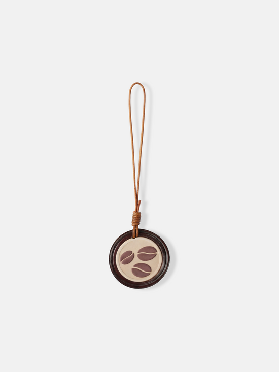 Selvane Coffee Bean Bag Charm: a circular leather medallion with a slim lanyard, featuring a subtle coffee bean motif.
