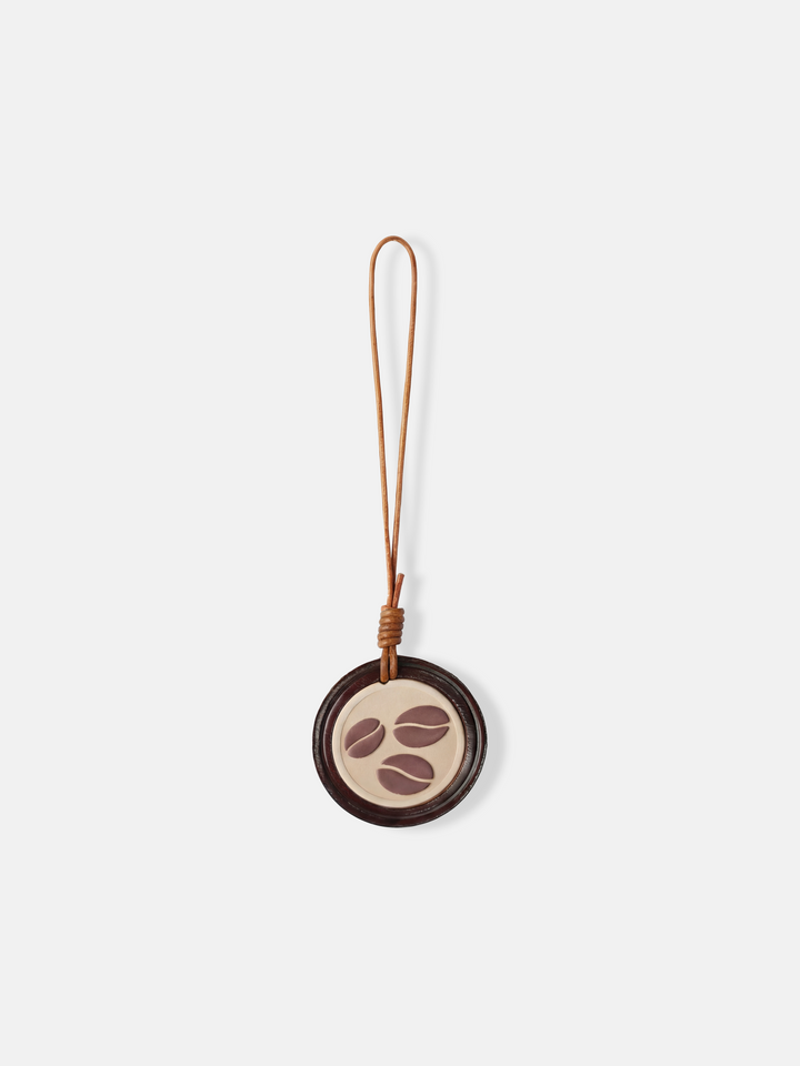 Selvane Coffee Bean Bag Charm: a circular leather medallion with a slim lanyard, featuring a subtle coffee bean motif.