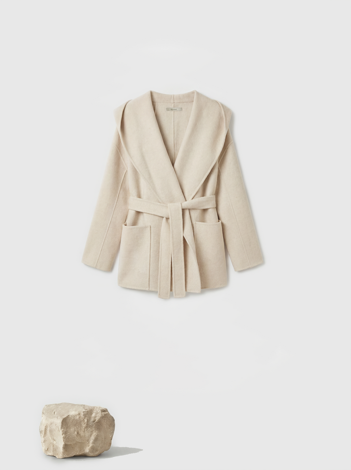 Full-length image of a cream wool belted overcoat with sculpted collar, self-tie belt, and oversized patch pockets, draped elegantly.
